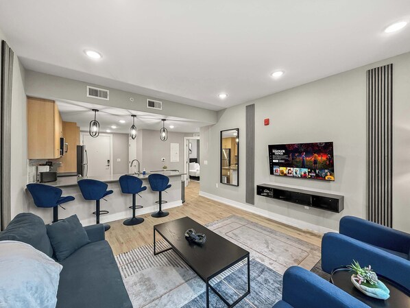 A modern living room with a sofa, blue chairs, a coffee table, and a TV wall-mounted above a fireplace.