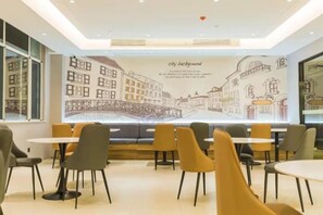 Un café avec des tables et des chaises disposées au premier plan, une fresque représentant un paysage urbain sur le mur au fond, et une fenêtre sur le côté gauche.