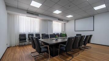 A conference room with a rectangular table, black chairs, a projector screen, and windows with curtains.