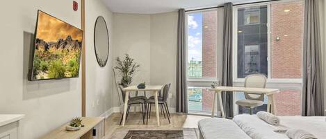 Una habitación de hotel moderna con una cama, un escritorio, una mesa de comedor y un ventanal grande.