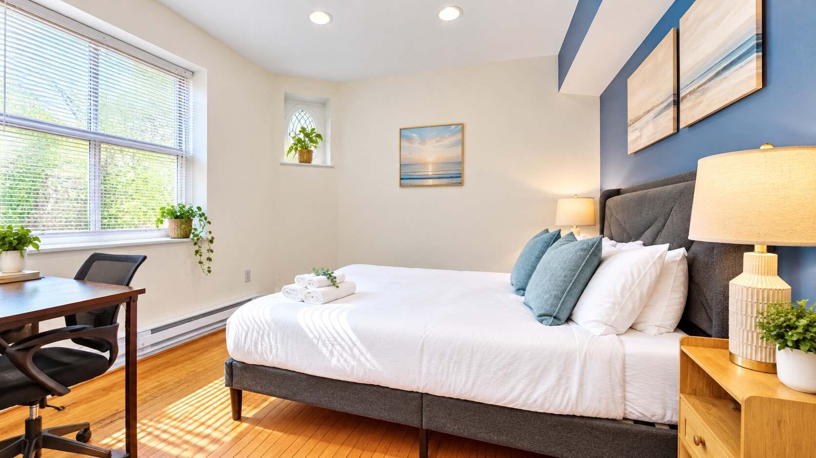 A neatly arranged bedroom with a bed, bedside tables, a desk, and a window with blinds.