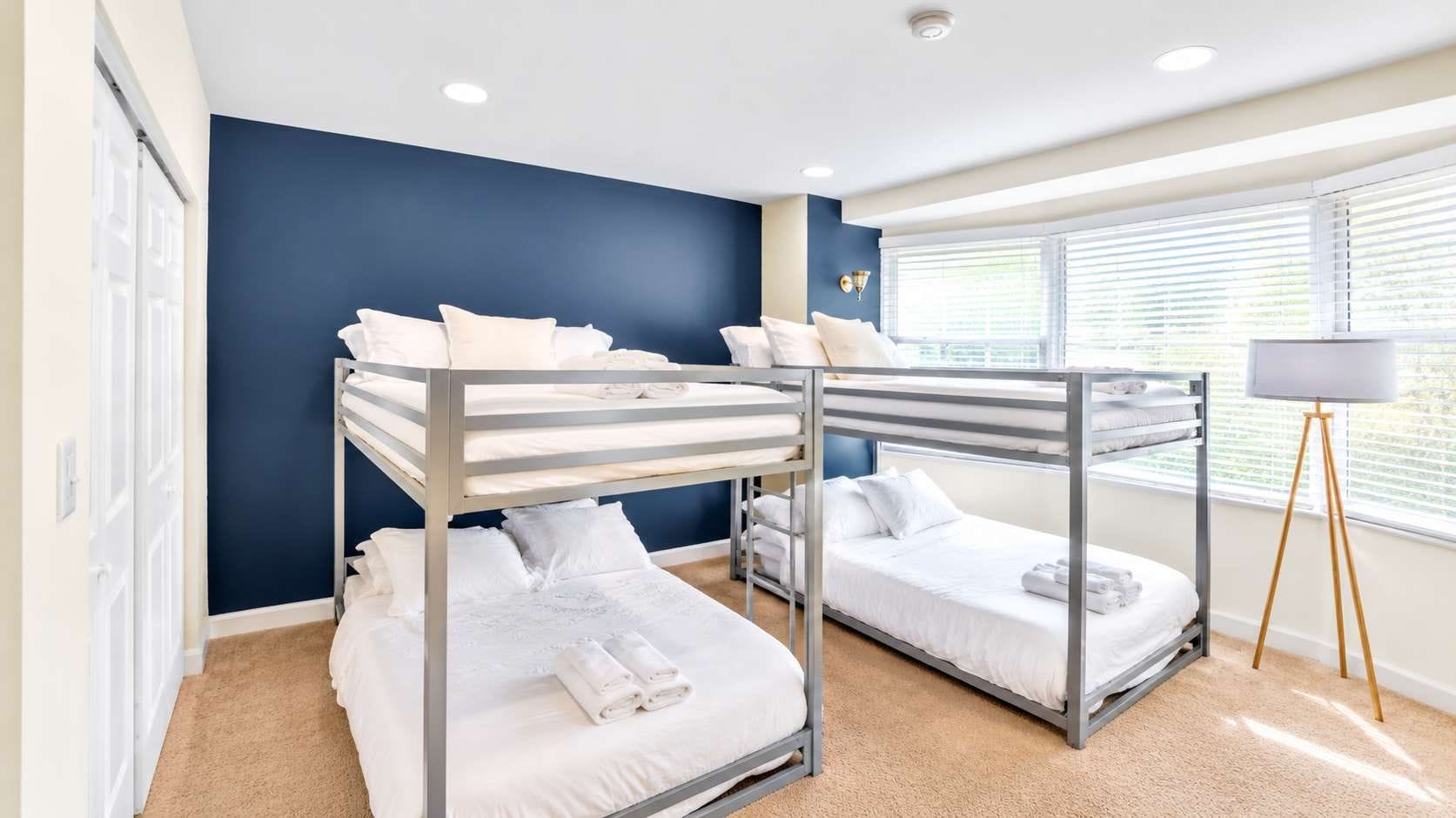 A room with bunk beds, a standing lamp, and a window with blinds.