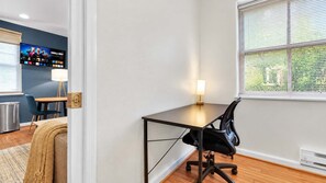 A hotel room with a desk, chair, and a television displaying a sports channel.