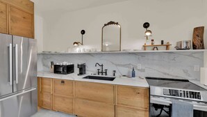 A modern kitchen with a stainless steel refrigerator, a built-in oven, a sink with a black faucet, and wooden cabinets. - Luxury 1BD | 1 Bed | South St (Philadelphia)
