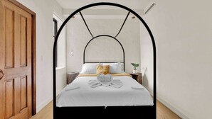 A bedroom with a bed under a black arch, white bedding, a wooden nightstand, a potted plant, and a wooden door. - Luxury 1BD | 1 Bed | South St (Philadelphia)