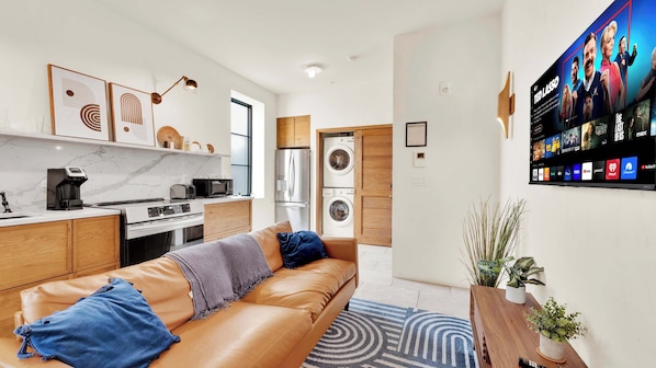 A modern apartment with a kitchen, a living area with a leather sofa, a TV wall, and a washing machine.