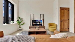 Een moderne woonkamer met een flatscreen televisie, een potplant, een gele fauteuil en een houten deur.
