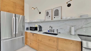 A modern kitchen with stainless steel appliances, wooden cabinets, a marble backsplash, and wall-mounted lighting.