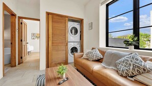 En moderne stue med en sofa, et sofabord med en plante, en vaskemaskine og et stort vindue med udsigt.