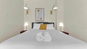 A neatly made bed with towels, a headboard, and two bedside lamps.