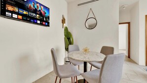 Et moderne spiseområde med et fladskærms-tv, der viser forskellige streamingtjenester, et rundt marmorbord og grå polstrede stole.