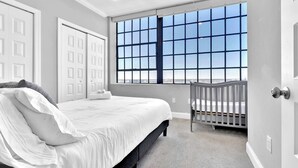 A bedroom with a large window, a bed, a crib, and white doors.
