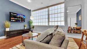 A modern living room with a flat-screen TV, a sofa, a coffee table, and a dining area with a table and chairs.