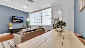 A modern living room with a TV, sofa, dining table, and large windows.