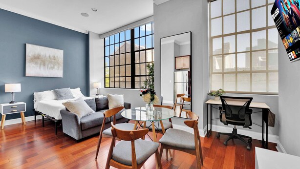 A modern living room with a sofa, chairs, a glass table, a desk, and a large window.