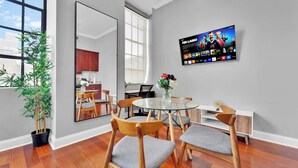 A modern living room with a dining area, a large TV mounted on the wall, and a potted plant.