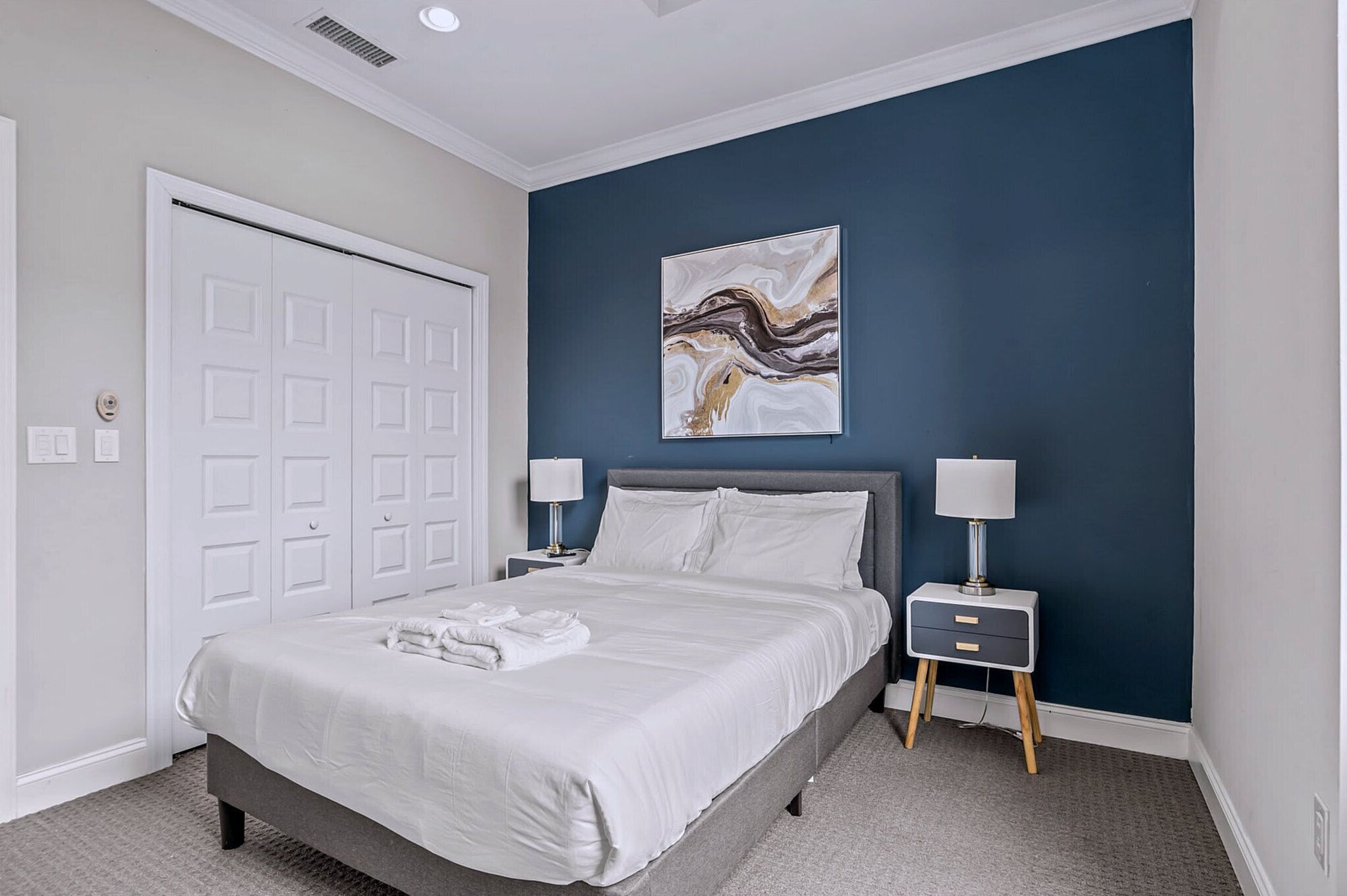 A bedroom with a bed, two bedside tables with lamps, a white door, and a blue accent wall.