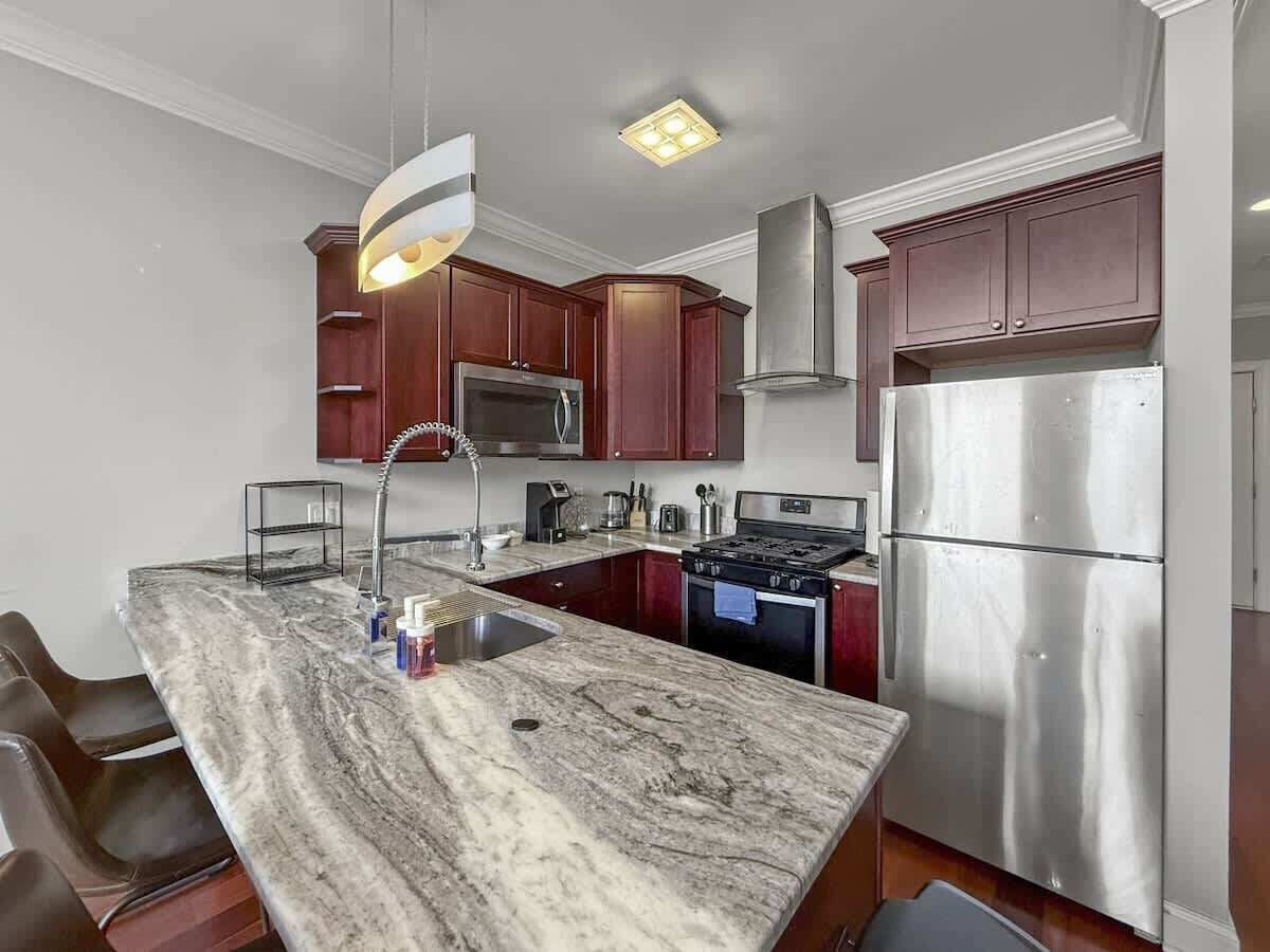 A modern kitchen with a marble countertop, stainless steel appliances, and dark wooden cabinets.