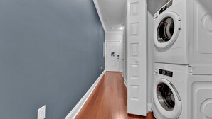 A laundry room with stacked washers and dryers, a wooden floor, and a gray wall.