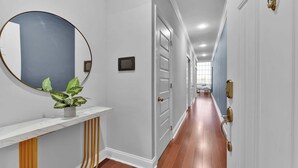 A hallway with a round mirror, a potted plant, a small table, and a door with a light switch.