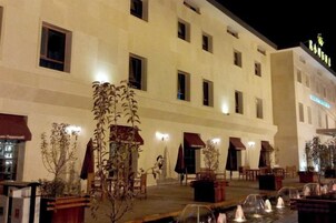 Fachada de hotel con múltiples ventanas, mobiliario exterior y una fuente de agua.