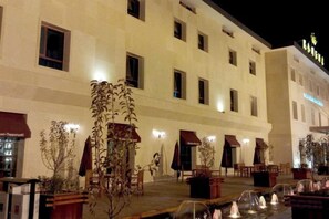 A hotel exterior with multiple windows, outdoor seating, and a water feature.