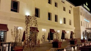 Une vue de l’extérieur d’un hôtel de nuit, avec de nombreuses fenêtres, des places assises en plein air et un élément décoratif aquatique.