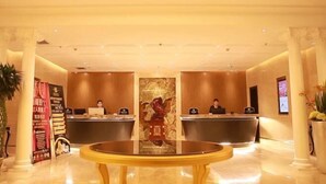 Un hall d’accueil d’hôtel avec une table ronde centrale, deux comptoirs d’accueil et une colonne décorative surmontée d’une statue.