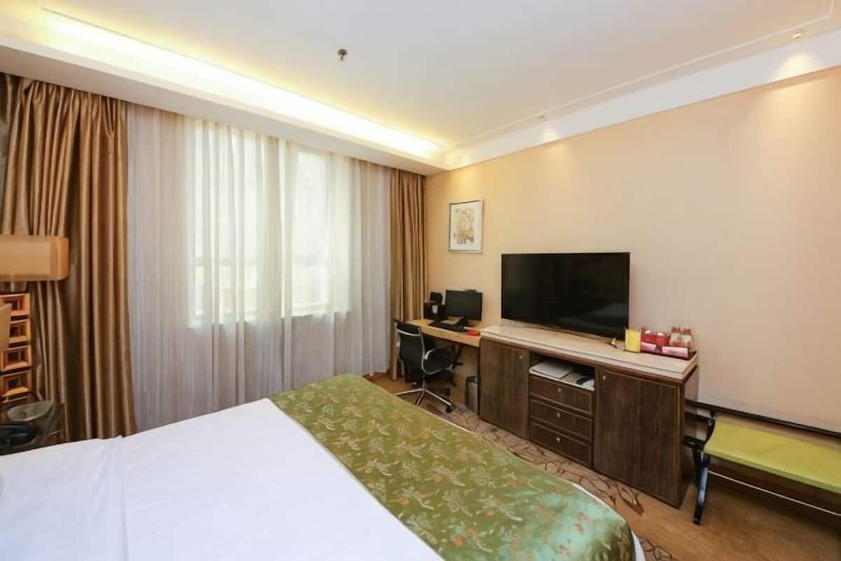 Une chambre d’hôtel avec un lit, un bureau, une télévision et une fenêtre avec des rideaux.