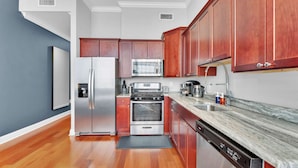 Una cocina con armarios de madera, electrodomésticos de acero inoxidable, encimera de mármol y lavavajillas.