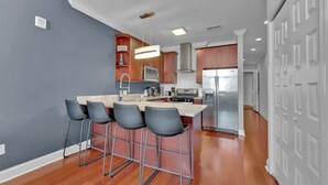 Una cocina moderna con una isla central, taburetes de bar, electrodomésticos de acero inoxidable y armarios de madera.
