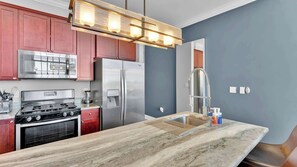 A kitchen with a gas stove, stainless steel refrigerator, and a marble countertop.