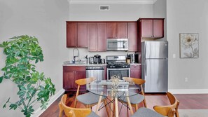 Cozinha moderna com armários de madeira, eletrodomésticos de aço inoxidável e uma mesa de jantar de vidro com cadeiras.