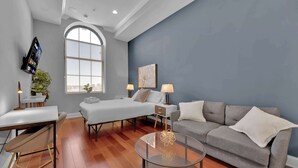 A modern living room with a bed, sofa, and coffee table, featuring a large window and a city view. - Luxury Studio | Northern Libs | 1 Bed | Onsite gym (Philadelphia)