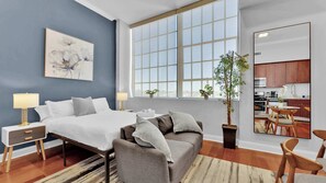 A modern bedroom with a large bed, bedside tables, a sofa, a potted plant, and a view of the kitchen. - Luxury Studio | Northern Libs | 1 Bed | Onsite gym (Philadelphia)