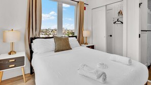 Habitación de hotel con una cama grande, dos mesitas de noche, un armario y vistas a la ciudad.