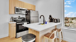 Una cocina moderna con electrodomésticos de acero inoxidable, encimera blanca y vistas a la ciudad a través de un amplio ventanal.