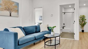 A modern living room with a blue sofa, a round glass coffee table, and a potted plant.