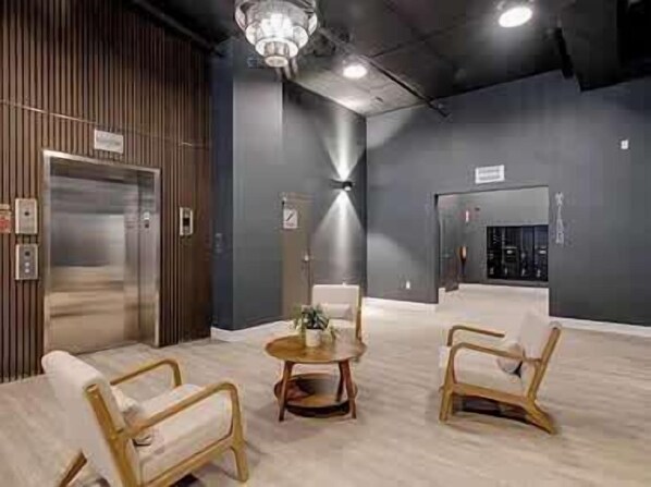 A modern lobby with a wooden reception desk, a chandelier, and a seating area with two chairs and a small round table.