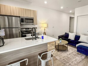 Una cocina moderna con electrodomésticos de acero inoxidable, una isla central con un lavamanos y una zona de estar con sofá y mesa de centro.