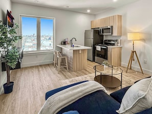 A modern kitchen with a large window, a refrigerator, microwave, and a small dining area. - Comfy 2BR for 4 | Philly Getaway Near Philly Spots (Philadelphia)