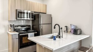 A compact kitchen with a microwave, stove, refrigerator, and a coffee maker. - Cozy 2BD Apt | Fishtown | Gym (Philadelphia)
