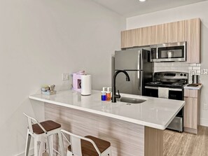 Een moderne keuken met een centraal eiland, roestvrijstalen apparatuur en een spatwand met houtstructuur.