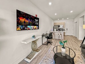 A modern living room with a flat-screen TV, a dining area, and a kitchen.