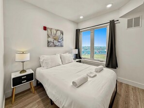 Habitació d'hotel amb un llit, una tauleta de nit amb una làmpada, una finestra amb cortines i un quadre a la paret.