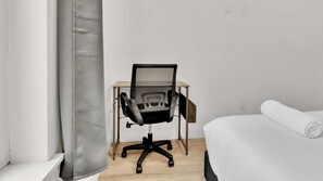 A room with a desk, a chair, a bed, and a window with a curtain.