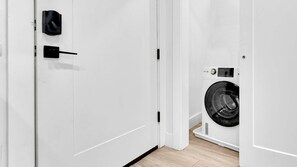 A clean, modern room with a white door, a black door handle, and a white washing machine. - 1BR Haven Independence Hall Oasis | Perfect for 2 (Philadelphia)