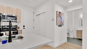A modern kitchen with a built-in microwave, stove, and sink. There is a small island with a faucet and a blue container. The kitchen has white cabinets and a wooden floor.