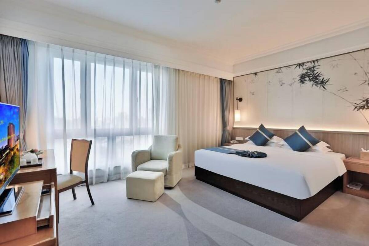 A modern hotel room with a large bed, a desk with a computer, a chair, and a TV.