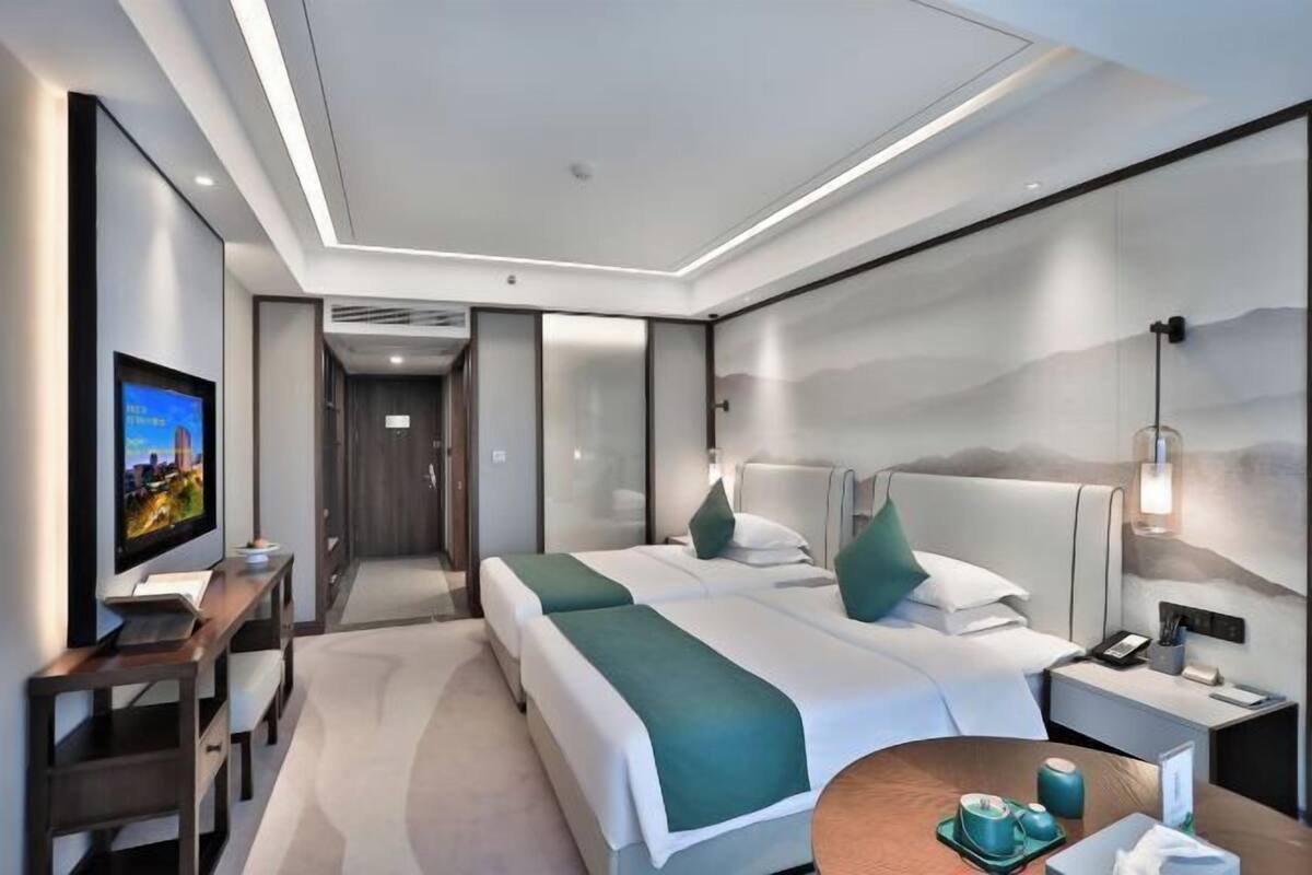A modern hotel room with two beds, a desk, a TV, and a bedside table with a lamp.